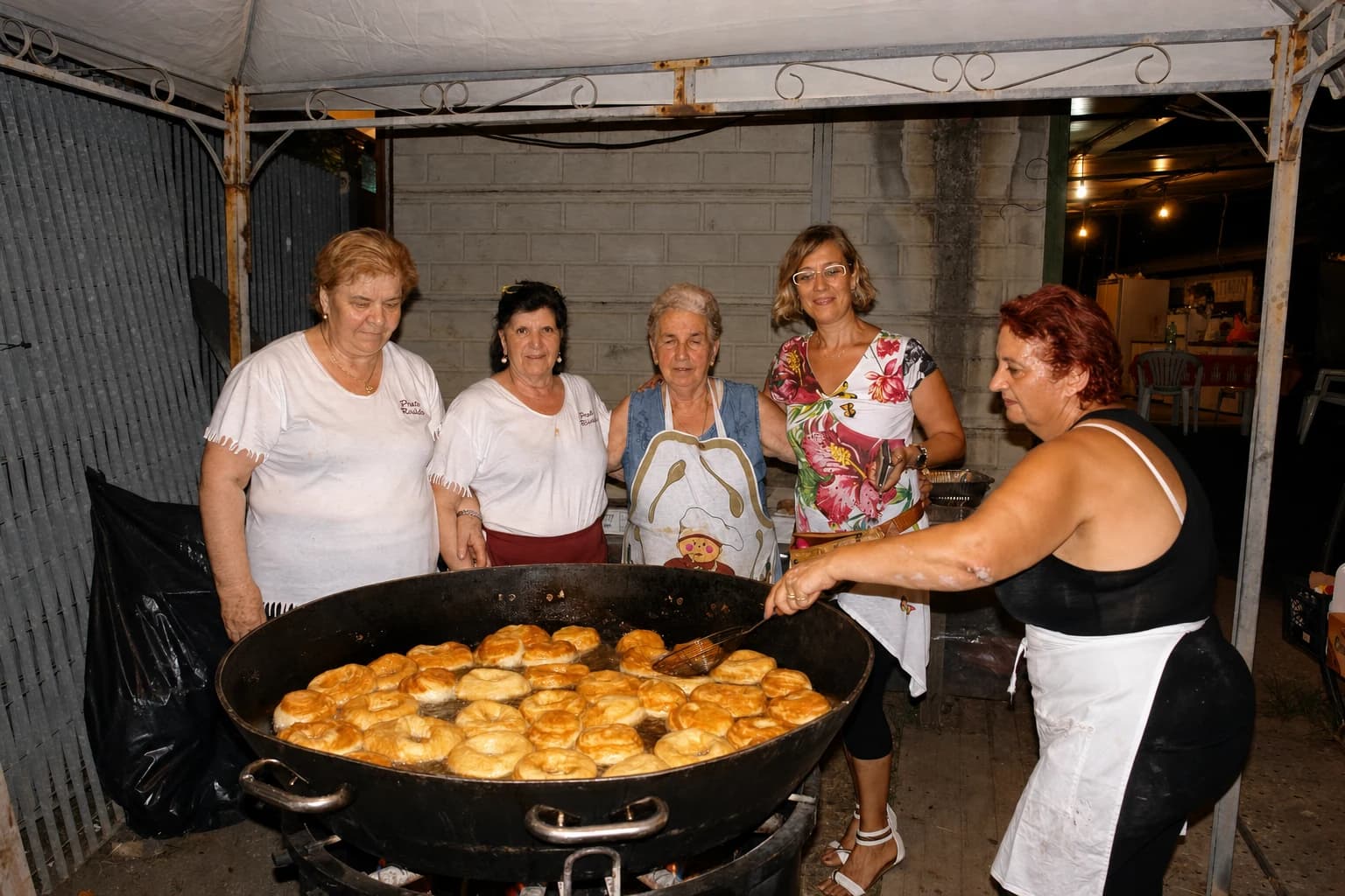 Cinque donne cucinano insieme davanti a una grande padella durante la festa del 2015.